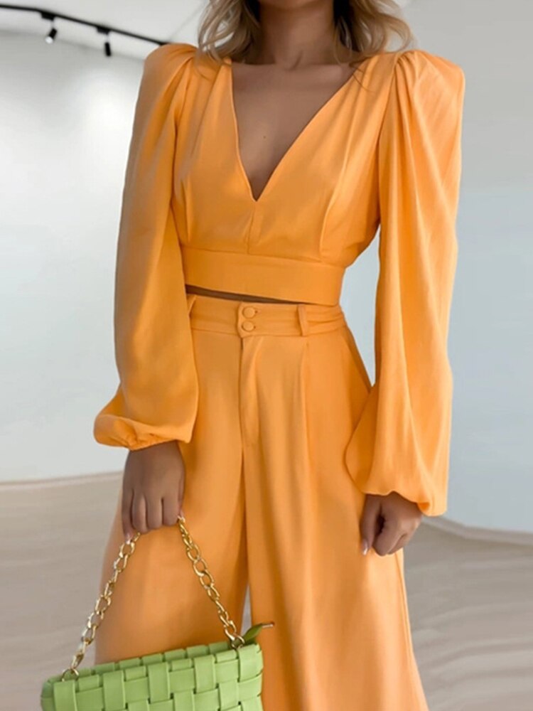 Tweedelige set in trendy oranje kleur. Deze set bestaat uit een top met charmante details en een bijpassende broek, waardoor je moeiteloos stijlvol voor de dag komt. De top heeft lange mouwen en een V-hals voor een trendy uitstraling, terwijl de broek is voorzien van rechte pijpen en een mid-rise taille voor comfort en veelzijdigheid.